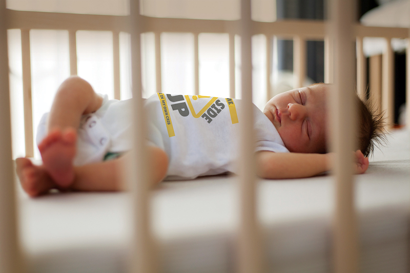 Baby in a crib with onesie that says,