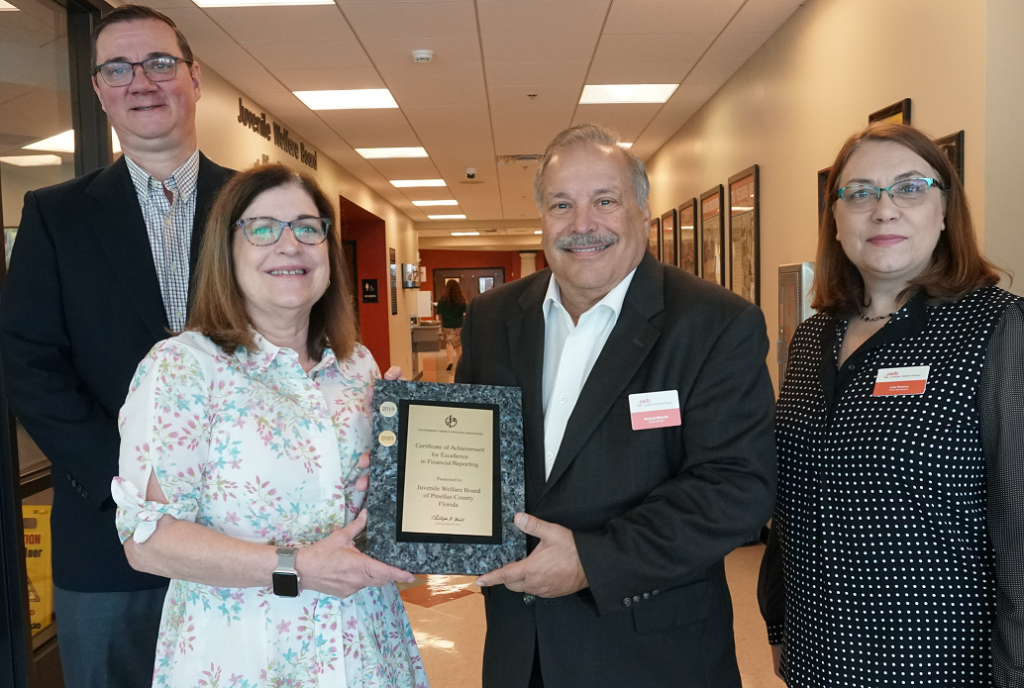 Juvenile Welfare Board Board chair and staff posing with GFOA's top award for Excellence in Financial Reporting: (l to r) Senior Accountant Richard Godfrey, Senior Manager of Accounting Lynn De la Torre, JWB Board Chair Mike Mikurak, and Fiscal Specialist Lilia Pletnev.
