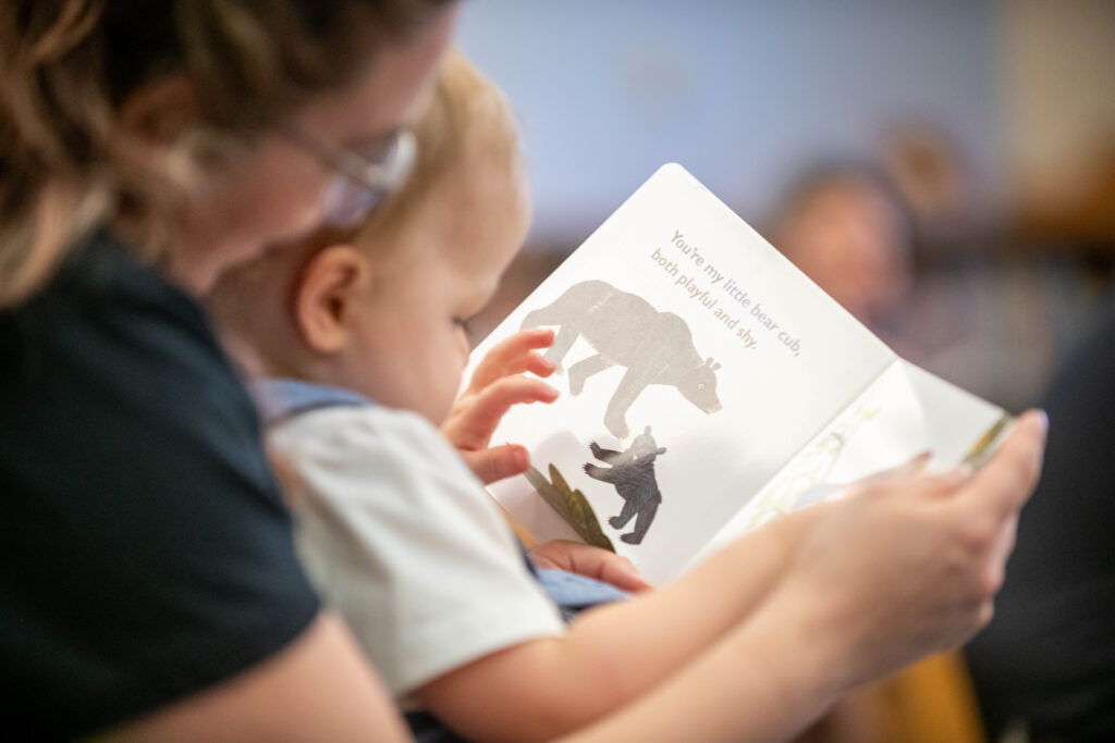 Mother holding baby in her lap while both look at the pages of the book being read aloud