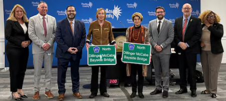 Kay Dillinger and Denise McCabe hold miniature versions of the Dillinger McCabe Bayside Bridge road sign that will honor their late husbands